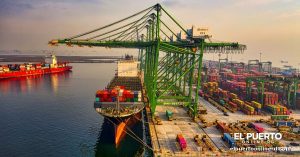 Grúas de pórtico verdes y un buque portacontenedores cargado de contenedores de colores en una terminal portuaria al atardecer.