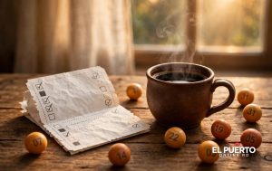 Ticket de lotería marcado sobre una mesa de madera junto a una taza de café humeante, con bolitas numeradas dispersas y luz dorada de mañana.