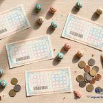 Vista cenital de tickets de lotería y bolitas numeradas de colores turquesa y coral sobre una mesa de madera clara, con monedas y un lápiz.