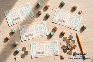 Vista cenital de tickets de lotería y bolitas numeradas de colores turquesa y coral sobre una mesa de madera clara, con monedas y un lápiz.