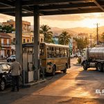 Estación de combustibles en el Caribe con un autobús, un camión cisterna y vehículos cargando combustible al atardecer